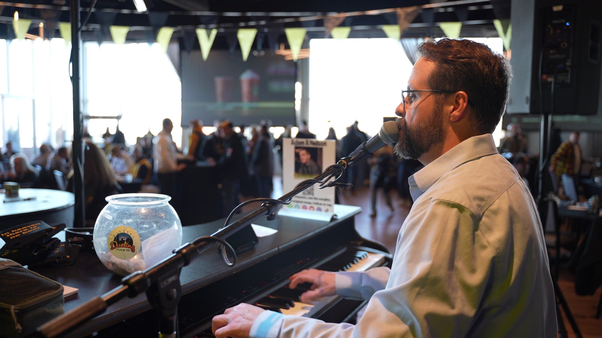 Midwest Dueling Pianos performer singing and playing piano with the audience in the background.